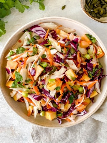 brown bowl of tropical mango coleslaw with mint next to it.