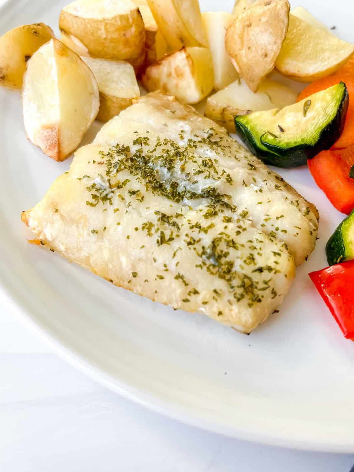 cod fillet with potatoes and vegetables on a white plate.