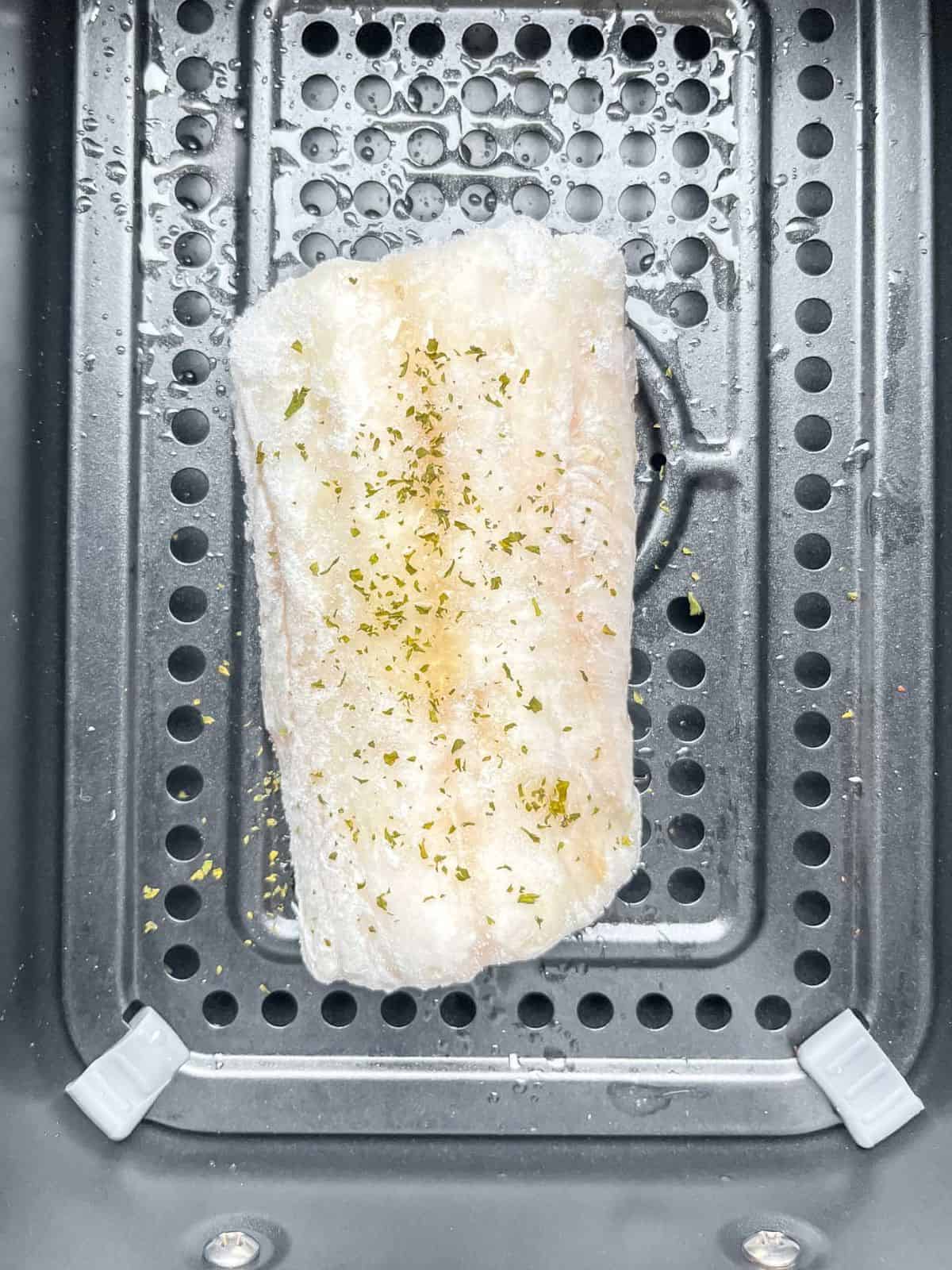frozen cod fillet in an air fryer basket.