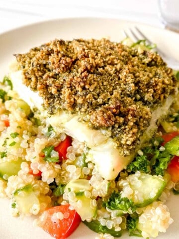 baked cod with a crust on top of a bed of quinoa and vegetables on a cream plate.